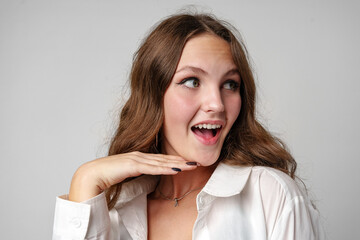 Excited Young Woman in White Blouse Reacting With Joyful Surprise Against a Grey Background