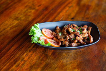 Garlic fried pork in a black plate placed on a wooden table, close-up photo, copy space