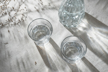 Two glasses with alcohol drink and bottle on table with aesthetic sunlight shadows, top view,...