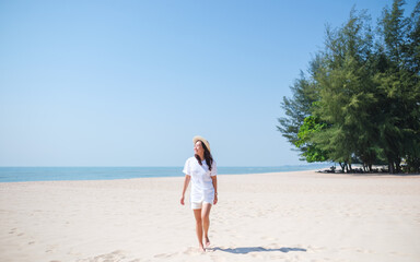Obraz premium Portrait image of a young woman while strolling on the beach with the sea and blue sky background