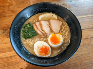 A bowl of ramen with rich brown broth is adorned with perfectly cooked toppings, creating an enticing visual and culinary delight. 