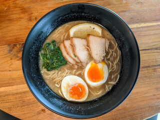 A bowl of ramen with rich brown broth is adorned with perfectly cooked toppings, creating an enticing visual and culinary delight. 