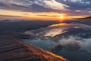 Sunrise over Polish Baltic Sea coast on a sandbank with reflection of clouds in the sea