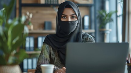 The gorgeous Muslim businesswoman wearing a burka is sitting at her desk working on her laptop computer in the office. The successful corporate CEO plans an investment strategy for an e-commerce