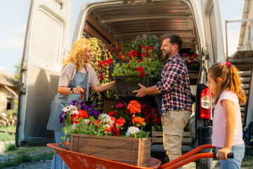 A family of three loading colorful flowers from a wheelbarrow into a delivery van for transport, highlighting their small family business. © DusanJelicic
