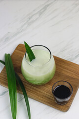 Cendol Pandan, one of popular Indonesian traditional drink, made from rice flour, pandan leaves extract, coconut milk and liquid of palm sugar. White marble background with copy space.