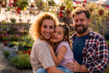 Fototapeta premium Heartwarming family moment as parents embrace their daughter, surrounded by the rich flora of their greenhouse.