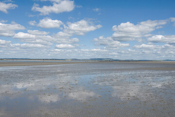 clouds and blue sky reflecting in the water on the beach at West Wittering West Sussex England