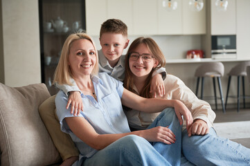 Lovely family relaxing on couch in living room. Little boy hugging his sister and mom. Cozy...