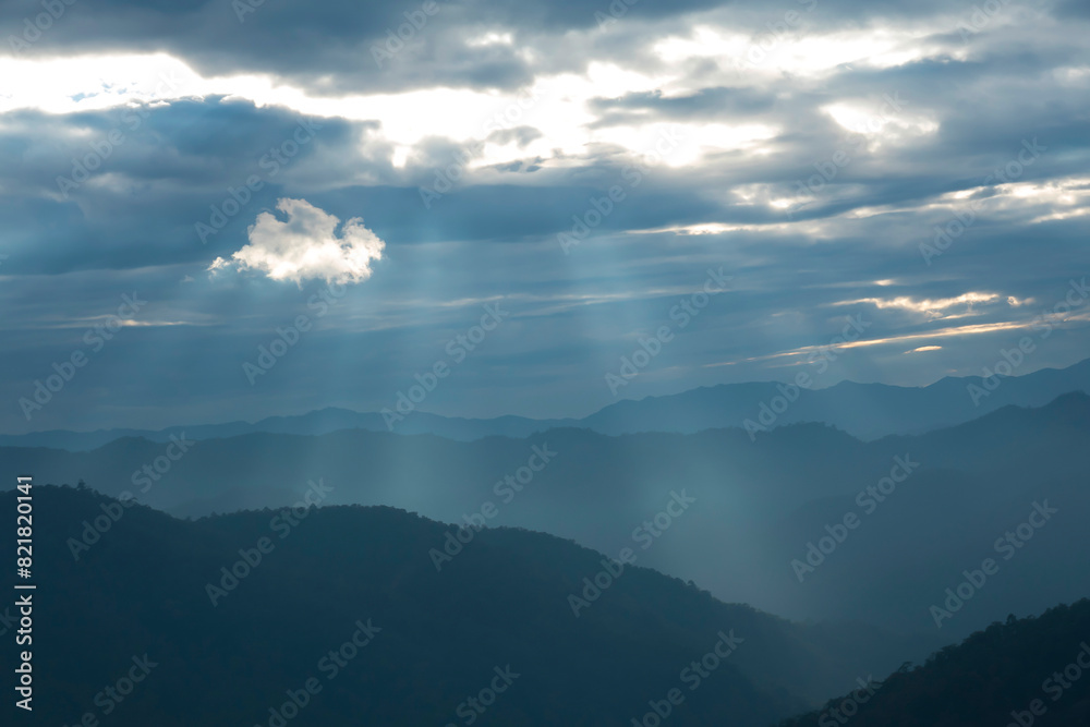 Wall mural sun rays filter through the clouds in hills of the valley illuminated by the sun's rays filtering th