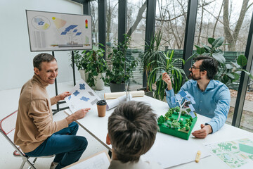 Happy businessman having discussion over solar panels project with colleagues sitting at desk