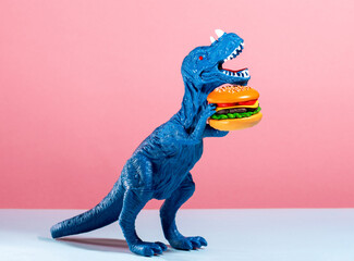 Close up blue dinosaur holding burger on pink and blue background.