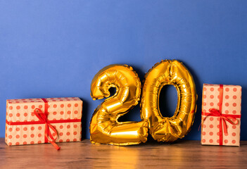 20 golden foil balloon numbers party decor on wooden table against blue wall. Birthday anniversary...