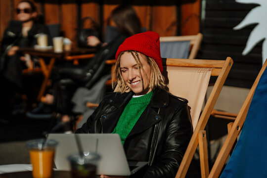 Smiling young woman using laptop sitting at sidewalk cafe on sunny day