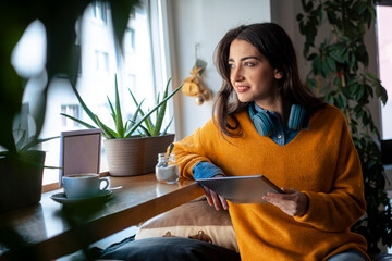 Thoughtful woman holding tablet PC sitting in cafe