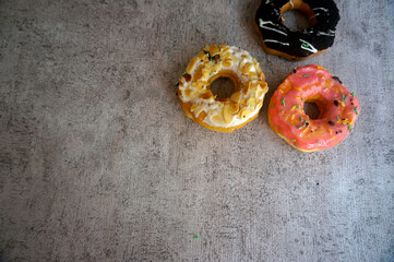 Top View Of Donuts With Almond Topping, Chocolate And Pink Icing With Sprinkles On Grey Background.