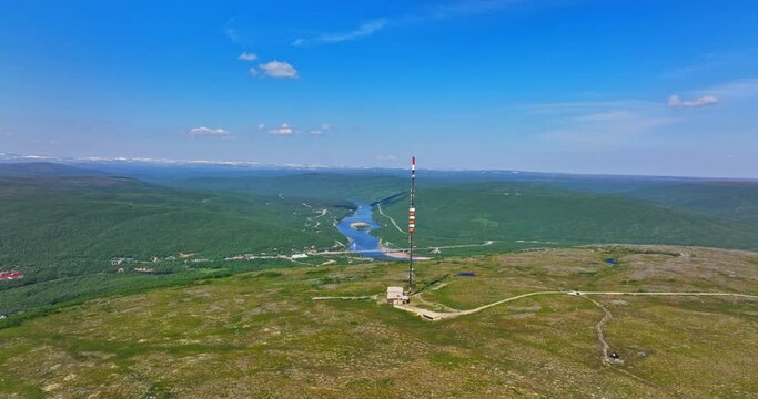 Aerial tracking shot of a radiotower on a mountain summit in sunny Utsjoki, Finland