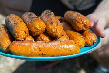 a man holds a blue plate on which there are grilled sausages, fast food, not healthy food