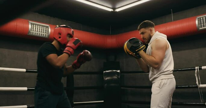 A teenager wearing a red protective helmet and gloves trains in a boxing ring with a coach.