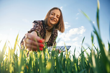 Touching the plant. Young woman is on the beautiful agricultural field at daytime