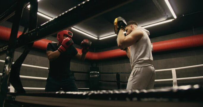 A teenager wearing a red protective helmet and gloves trains in a boxing ring with a coach.