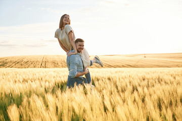 Having fun, man is holding woman. Lovely beautiful couple are together on the agricultural field