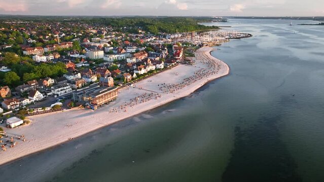 Aerial footage flying over Baltic Sea resort of Laboe, showcasing beach dotted with hooded beach chairs, marina and view of Kiel Bay (Kieler F&ouml;rde).