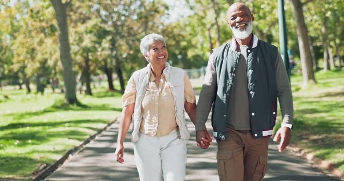 Love, happy and senior couple holding hands while walking in park with conversation, trust or bonding in nature. Interracial marriage, care or elderly people in forest with retirement, fun or travel