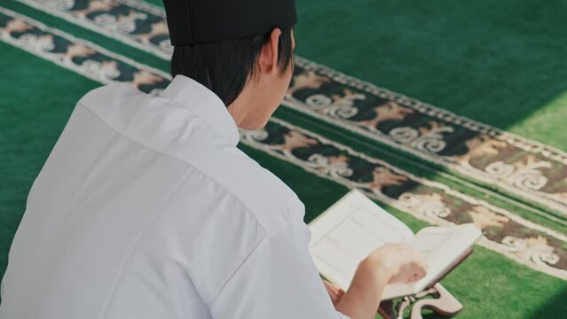 Rear View Of Young Asian Muslim Mand Reciting Holy Quran With Sunlight From Window 