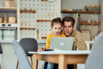 A surprised-looking dad and his daughter watching a video on a laptop together