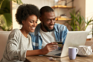 Naklejka premium A happy young couple making a credit card payment on a laptop together at home.