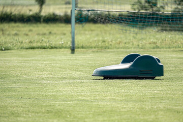 An autonomous battery lawn mower cuts the grass on an amateur football field.
