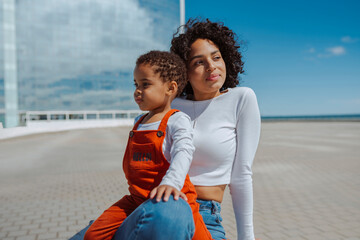 Young multiracial mother and daughter with curly afro hairstyle, enjoying together outdoors during spring, summer vacations. Lifestyle, maternity concept.