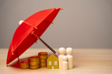 Property and family insurance concept. Miniature figures of a family stand near a house with coins under a red umbrella. Safety life
