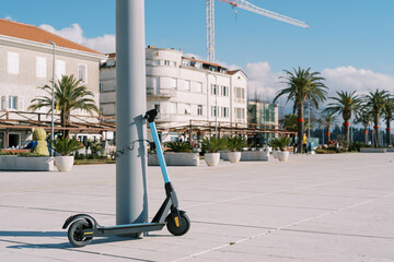 Blue rental electric scooter fastened to a pole on the promenade
