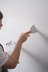 Man removes holes and bumps on the wall with a spatula and plaster