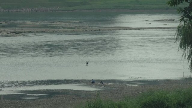 During the dry season of the Jialing River, there are people standing in the water fishing