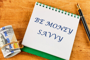 Savings concept,Text Be money savvy on a notepad near money and a fountain pen on an abstract background