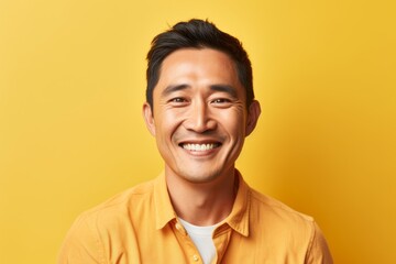 Obraz premium Portrait of a tender asian man in his 40s smiling at the camera while standing against pastel yellow background