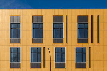 Wall of commercial building with large windows and yellow metal ventilated facades. Fragment of building for design on construction or architectural theme, for web site, landing page
