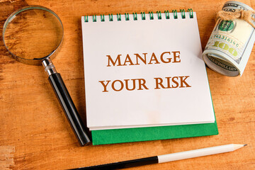 Business and manage your risk concept. Concept word Manage your risk on a notebook with a magnifying glass and a roll of money on a papyrus background