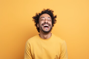 Portrait of a satisfied indian man in his 30s laughing on pastel yellow background