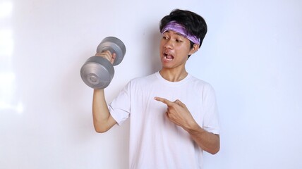 Excited young man in white shirt is training his arms lifting and pointing at the barbell
