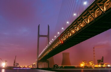 Majestic illuminated HuangPu bridge spans over a vast expanse of water in the evening