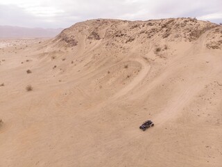 Off-road vehicle driving along a desert terrain with mountains in the background