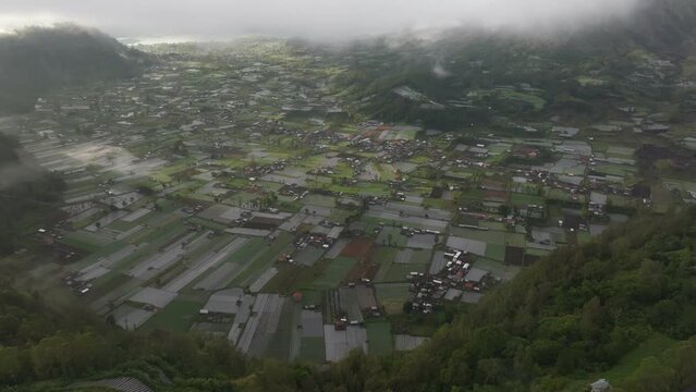 Aerial view of farmland, village, mountain, valley, and clouds in Batur with Pinggan, Bali, Indonesia.