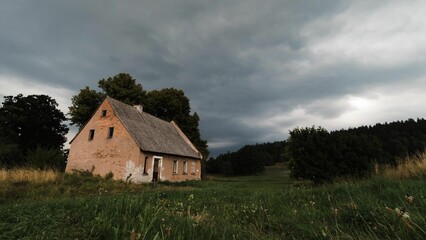 Aged brick house with a traditional thatched roof situated in a rural fieldscape
