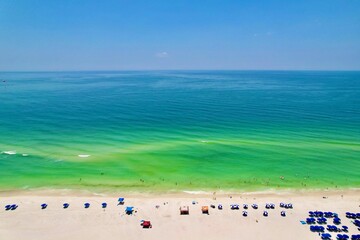 Aerial shot of a lively beach with numerous umbrellas dotting the shoreline.