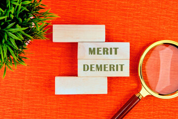 Merit and Demerit. fine concept. Text Demerit or merit symbol. on wooden blocks with a flower and a magnifying glass in the composition . Beautiful orange background