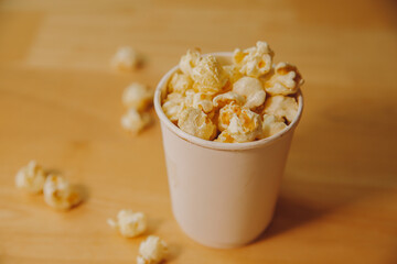 A bucket of popcorn, top-view, warm colors, light brown wooden background, flat lay, daylight macro...